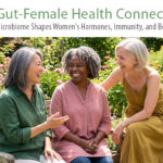 gut health for women: Three diverse women in their 50s and 60s laughing together in a summer garden, representing the connection between community, wellness, and women's health across every life stage